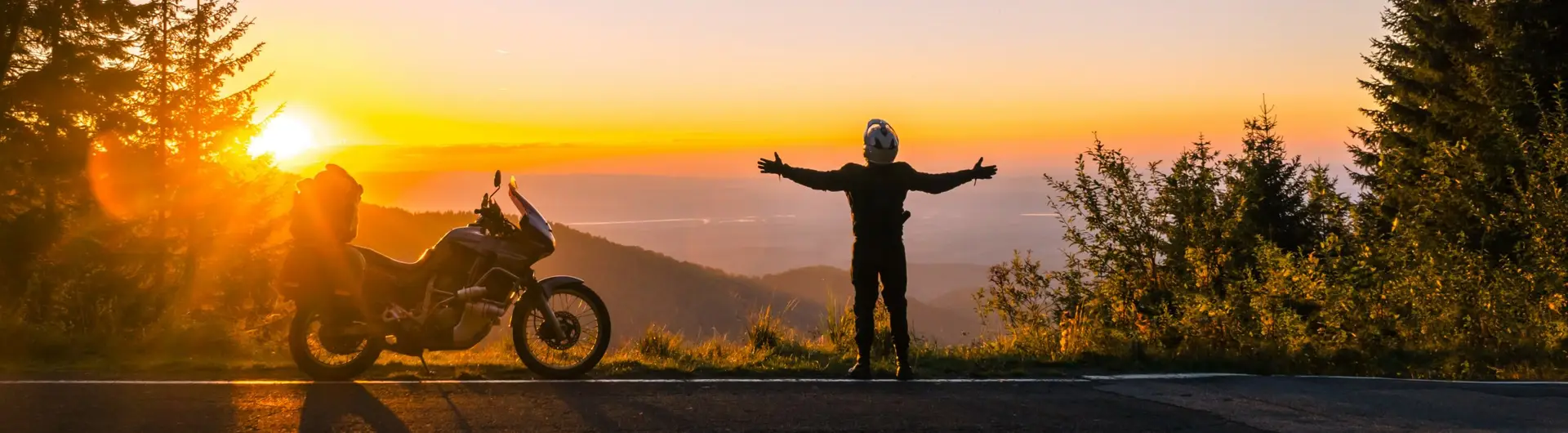 Motard devant un beau couché de soleil. Il écarte les bras et adore ce moment devant le soleil couchant.